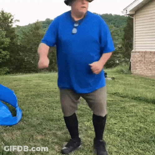 A Man In A Blue Shirt And Hat Is Dancing In A Yard GIF