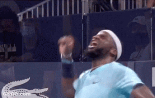 A Man In A Blue Shirt And Headband Is Standing On A Tennis Court With His Arms Outstretched . GIF
