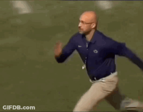 A Man In A Blue Shirt And Khaki Pants Is Running Across A Field . GIF