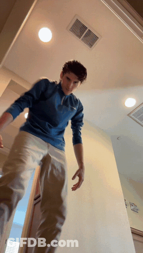 A Man In A Blue Shirt And Khaki Pants Is Standing In A Doorway GIF
