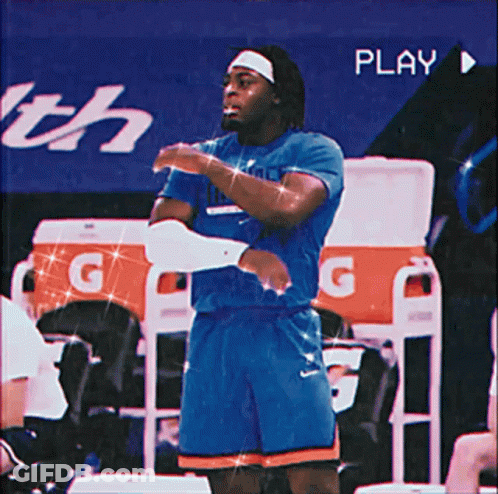 A Man In A Blue Shirt And Orange Shorts Is Standing In Front Of An Orange Gatorade Cooler GIF