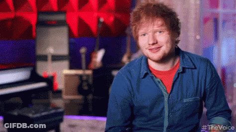 A Man In A Blue Shirt And Red T-Shirt Is Smiling In A Recording Studio . GIF