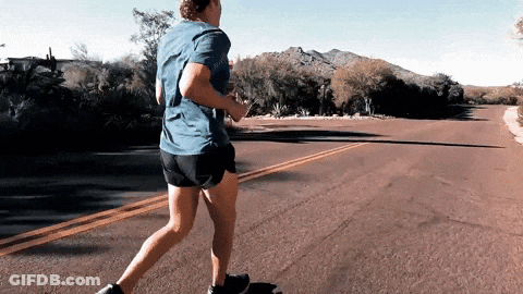 A Man In A Blue Shirt And Shorts Is Running Down A Road GIF