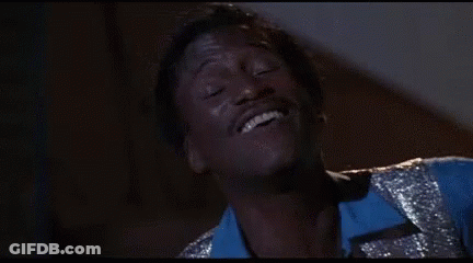 A Man In A Blue Shirt And Silver Vest Is Smiling With His Eyes Closed . GIF