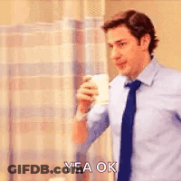 A Man In A Blue Shirt And Tie Is Holding A Cup Of Coffee And Saying `` Yea Ok '' . GIF
