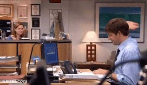 A Man In A Blue Shirt And Tie Is Sitting At A Desk In An Office . GIF