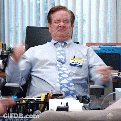 A Man In A Blue Shirt And Tie Is Sitting At A Desk In An Office Making A Funny Face . GIF
