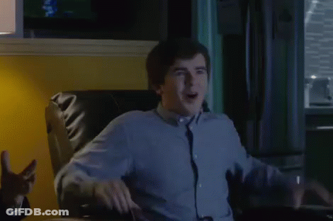 A Man In A Blue Shirt And Tie Is Sitting In A Chair And Making A Funny Face . GIF