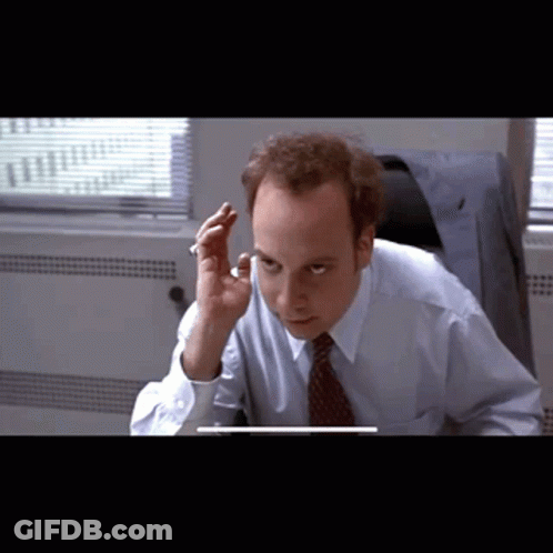 A Man In A Blue Shirt And Tie Is Sitting In Front Of A Computer GIF