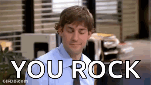 A Man In A Blue Shirt And Tie Is Sitting In Front Of A Sign That Says You Rock . GIF