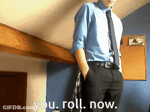 A Man In A Blue Shirt And Tie Is Standing In Front Of A Wall That Says You Roll Now GIF