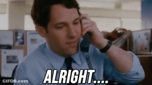 A Man In A Blue Shirt And Tie Is Talking On A Telephone And Saying `` Alright '' . GIF