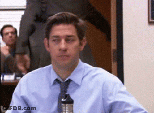 A Man In A Blue Shirt And Tie Sits At A Table GIF
