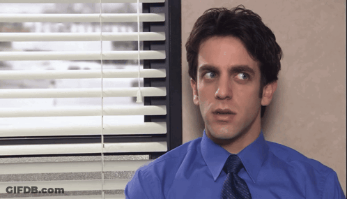 A Man In A Blue Shirt And Tie Stands In Front Of A Window GIF