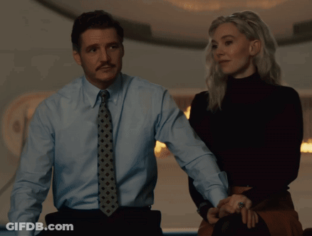 A Man In A Blue Shirt And Tie Stands Next To A Woman In A Black Turtleneck GIF