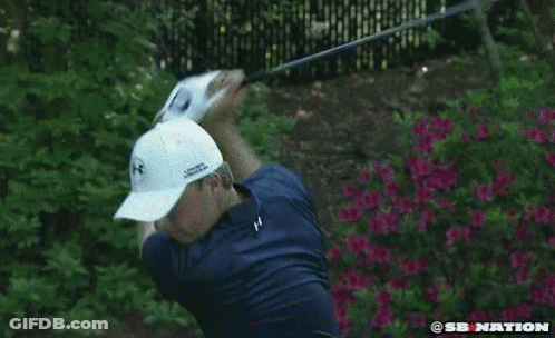 A Man In A Blue Shirt And White Hat Is Swinging A Golf Club . GIF