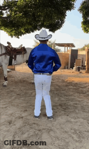 A Man In A Blue Shirt And White Pants Is Standing In Front Of A Horse GIF