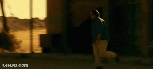 A Man In A Blue Shirt And White Pants Is Walking Down A Street . GIF