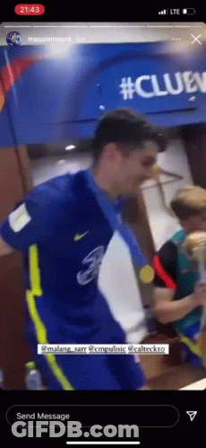 A Man In A Blue Shirt And Yellow Pants Is Holding A Medal Around His Neck . GIF