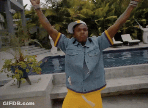 A Man In A Blue Shirt And Yellow Shorts Is Standing In Front Of A Swimming Pool GIF