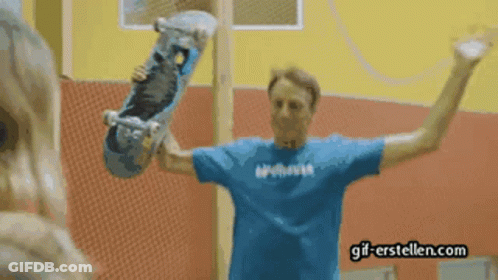 A Man In A Blue Shirt Holding A Skateboard With Gif-Erstellen.com Written On The Bottom GIF