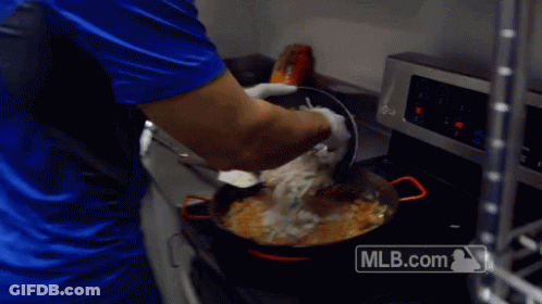 A Man In A Blue Shirt Is Cooking In A Kitchen With A Mlb.com Logo On The Stove GIF