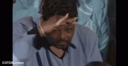 A Man In A Blue Shirt Is Covering His Face With His Hand While Sitting At A Table . GIF