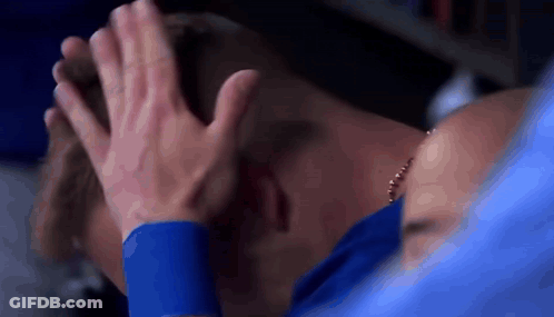 A Man In A Blue Shirt Is Covering His Face With His Hands While A Woman Holds His Head . GIF