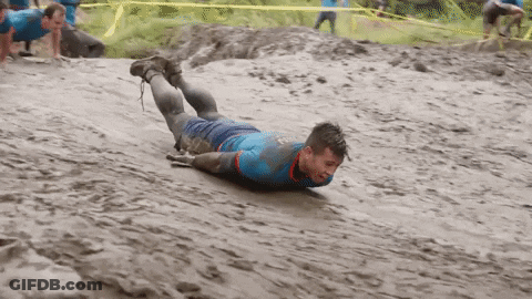 A Man In A Blue Shirt Is Crawling In The Mud . GIF