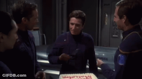 A Man In A Blue Shirt Is Cutting A Cake That Says Happy Birthday GIF