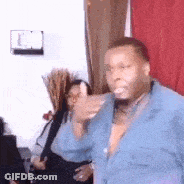 A Man In A Blue Shirt Is Dancing In A Living Room With A Woman In The Background . GIF