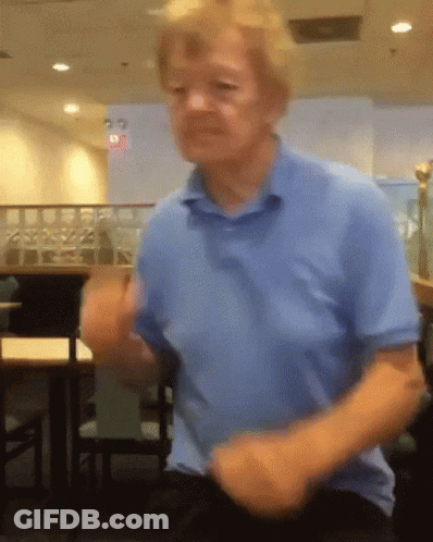 A Man In A Blue Shirt Is Dancing In A Room With Tables And Chairs GIF