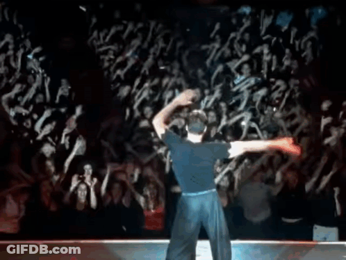 A Man In A Blue Shirt Is Dancing In Front Of A Crowd Of People . GIF