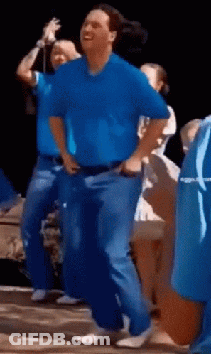 A Man In A Blue Shirt Is Dancing In Front Of A Group Of People GIF