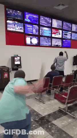 A Man In A Blue Shirt Is Dancing In Front Of A Wall Full Of Televisions GIF
