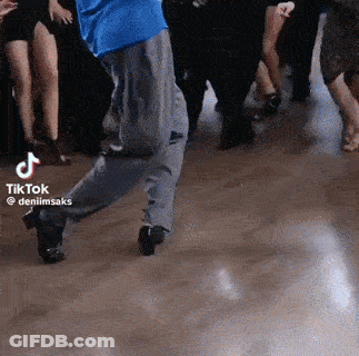 A Man In A Blue Shirt Is Dancing With A Crowd Of People Behind Him . GIF