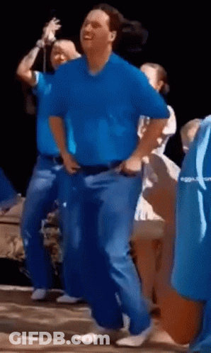 A Man In A Blue Shirt Is Dancing With A Group Of People . GIF