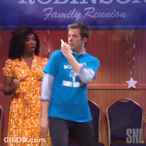 A Man In A Blue Shirt Is Dancing With A Woman In An Orange Dress In Front Of A Sign That Says Family Reunion GIF
