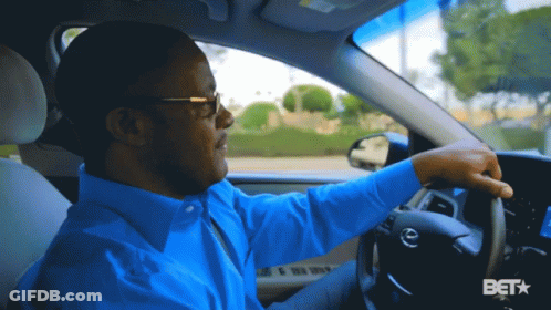 A Man In A Blue Shirt Is Driving A Car With A Bet Logo In The Corner GIF