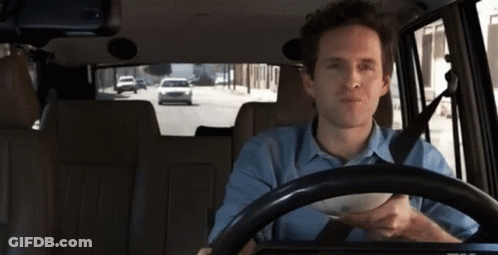 A Man In A Blue Shirt Is Driving A Car With A Bowl In His Hand GIF