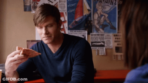 Man In Blue Shirt Eating Pizza In Front Of Reward Poster GIF