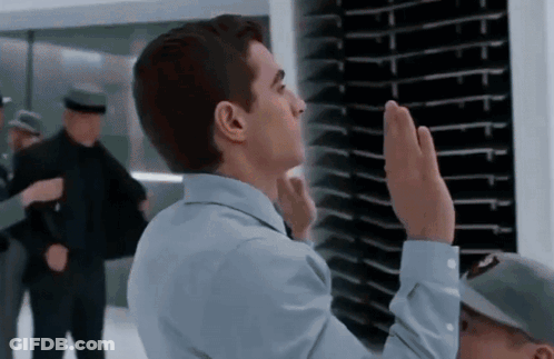 A Man In A Blue Shirt Is Giving A High Five In Front Of A Wall GIF