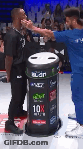 A Man In A Blue Shirt Is Giving Another Man A High Five In Front Of A Trash Can . GIF