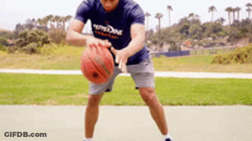 A Man In A Blue Shirt Is Holding A Basketball In His Hands On A Court . GIF
