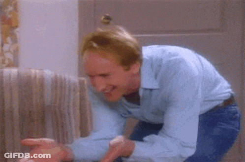 A Man In A Blue Shirt Is Holding A Cat In His Arms In A Living Room GIF