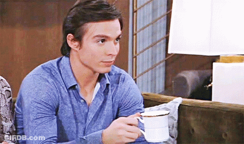 A Man In A Blue Shirt Is Holding A Cup Of Coffee . GIF