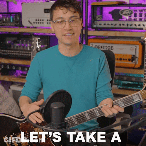 A Man In A Blue Shirt Is Holding A Guitar In Front Of A Microphone With The Words Let 'S Take A Below Him GIF
