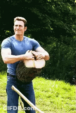 A Man In A Blue Shirt Is Holding A Large Log And A Shovel GIF