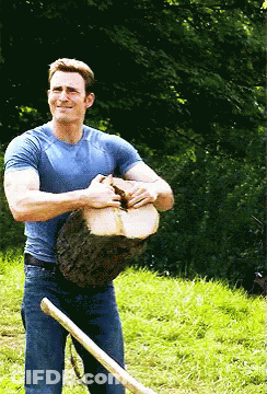 A Man In A Blue Shirt Is Holding A Large Log And A Shovel GIF