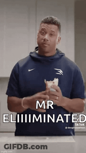 A Man In A Blue Shirt Is Holding A Sandwich In His Hands . GIF